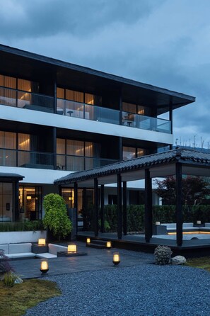 A modern multi-story building with a covered outdoor seating area and a well-maintained garden.