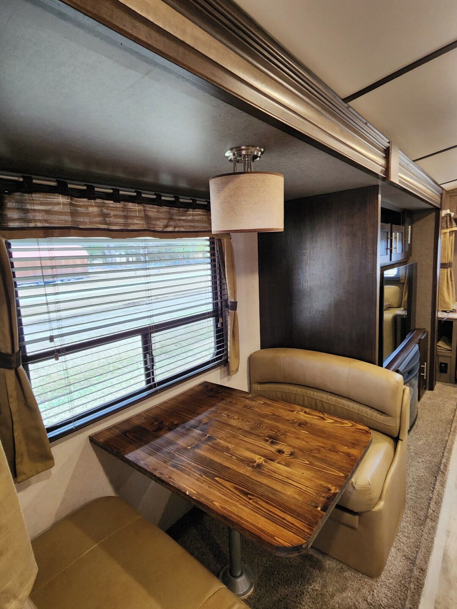 Een compact interieur van een camper met een eettafel, gestoffeerde zittingen, een raam met verduistering en een plafondlamp.