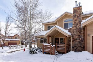 A two-story house with a stone chimney, a covered porch, and a snow-covered driveway. - Corner Home-Private Garage-Clubhouse | Sleeps 12 | Moose Mgmt 5672 (Park City)