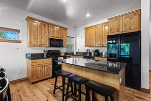 Eine moderne Küche mit Holzschränken, einem schwarzen Kühlschrank, einer Mikrowelle und einer Kaffeemaschine.