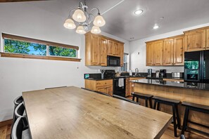 A modern kitchen with wooden cabinets, a large island, and a window with a view of trees. - Corner Home-Private Garage-Clubhouse | Sleeps 12 | Moose Mgmt 5672 (Park City)