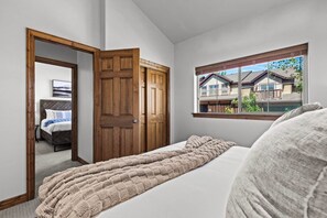 Ein Schlafzimmer mit einem Bett, einem Fenster mit Blick auf Häuser und einer Holztür.