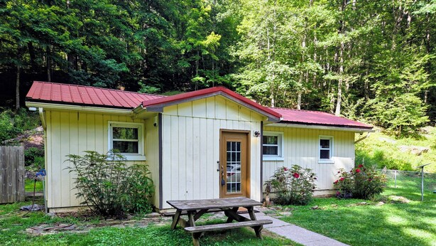 A small, single-story house with a red roof, a front door, and a wooden bench in front. - Escape the hustle and reconnect with nature at Outpost, your stay tucked along the borders of Shawnee State Forest. Whether you're seeking a solo retreat, a romantic getaway, or a  weekend with friends, this spot offers a blend of woods & comfort. (West Portstmouth)