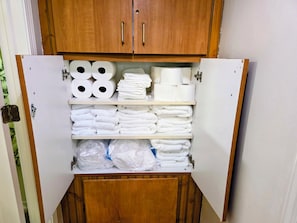 Een opslagkast met planken, gevuld met toiletpapier, handdoeken en plastic zakken.
