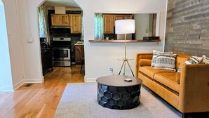 A modern living room with a round coffee table, a sofa, and a kitchen visible through an archway. - Escape the hustle and reconnect with nature at Outpost, your stay tucked along the borders of Shawnee State Forest. Whether you're seeking a solo retreat, a romantic getaway, or a  weekend with friends, this spot offers a blend of woods & comfort. (West Portstmouth)