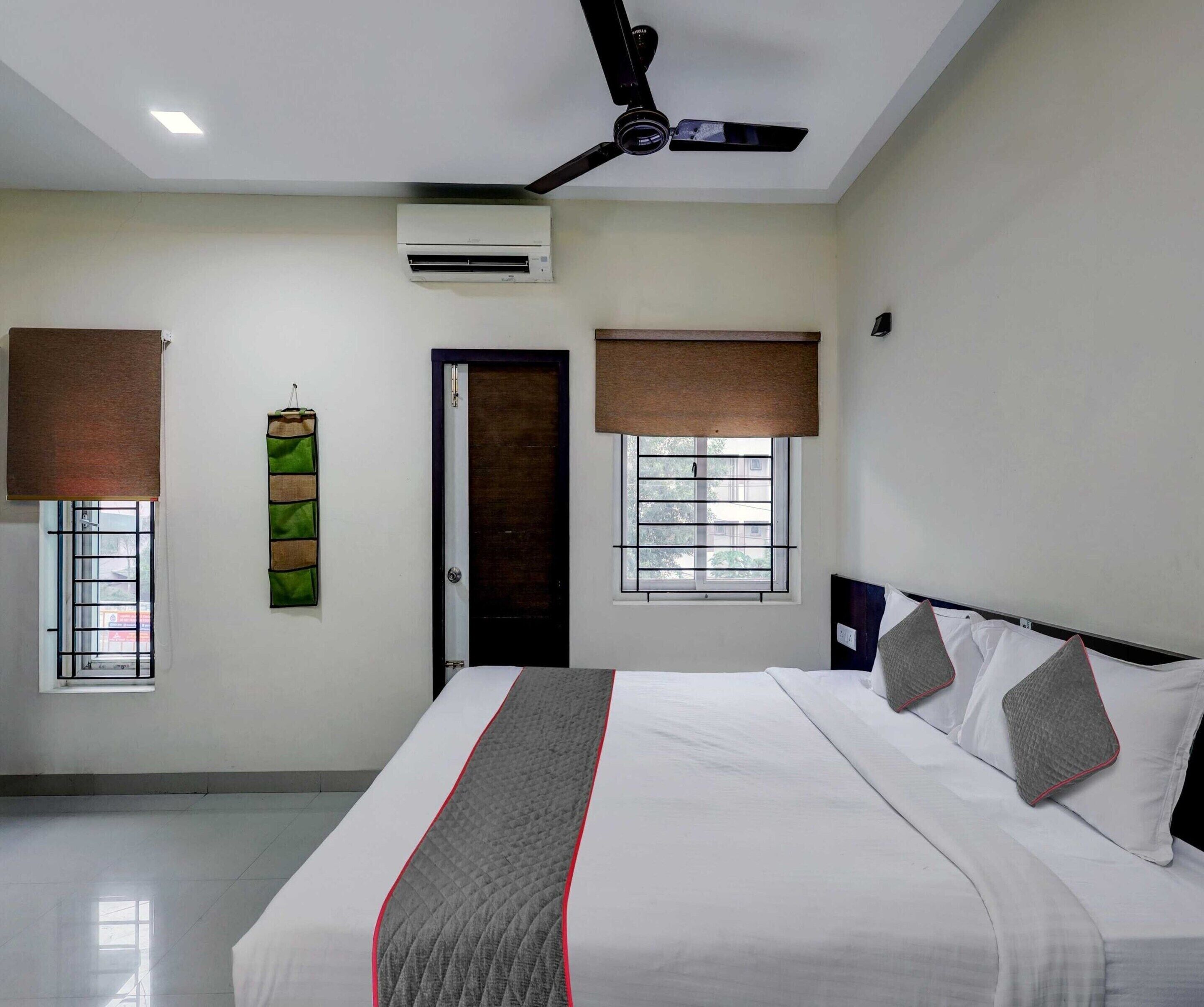 Une chambre d’hôtel équipée d’un lit, d’un ventilateur de plafond, d’un appareil de climatisation et de fenêtres avec des stores.