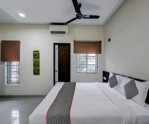 A hotel room with a bed, a ceiling fan, an air conditioning unit, and windows with blinds.