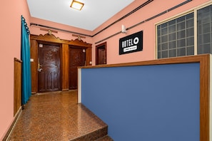 A hotel reception area with a blue counter, wooden doors, and a sign indicating it is serviced by OYO.