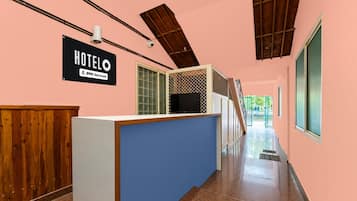 A hotel reception area with a wooden reception desk, a sign indicating 'HOTEL OYO-Serviced', and a staircase leading to an upper level.