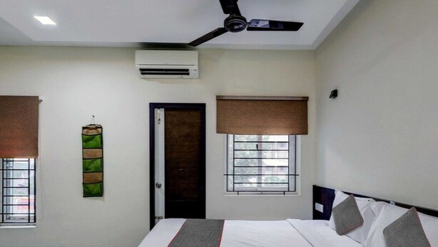 A bedroom with a bed, a ceiling fan, an air conditioning unit, and windows with blinds.