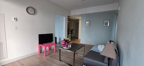 Un salon avec un téléviseur à écran plat, un fauteuil rose, une table basse, un canapé et une lampe.