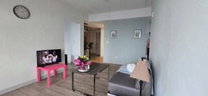 A living room with a television, a pink chair, a table with flowers, and a sofa.