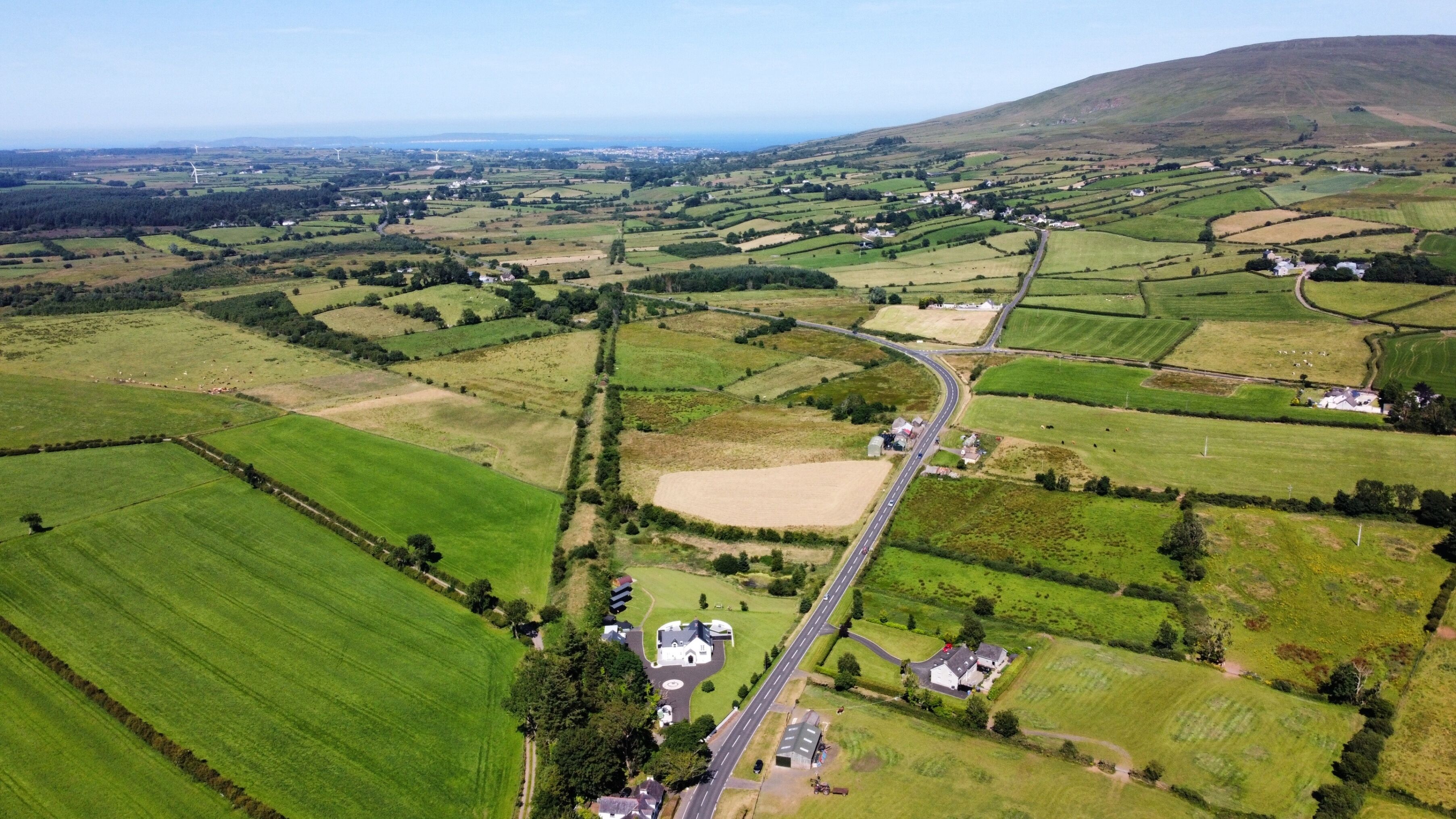 Vista aérea de un paisaje rural con campos, un camino sinuoso y casas dispersas.