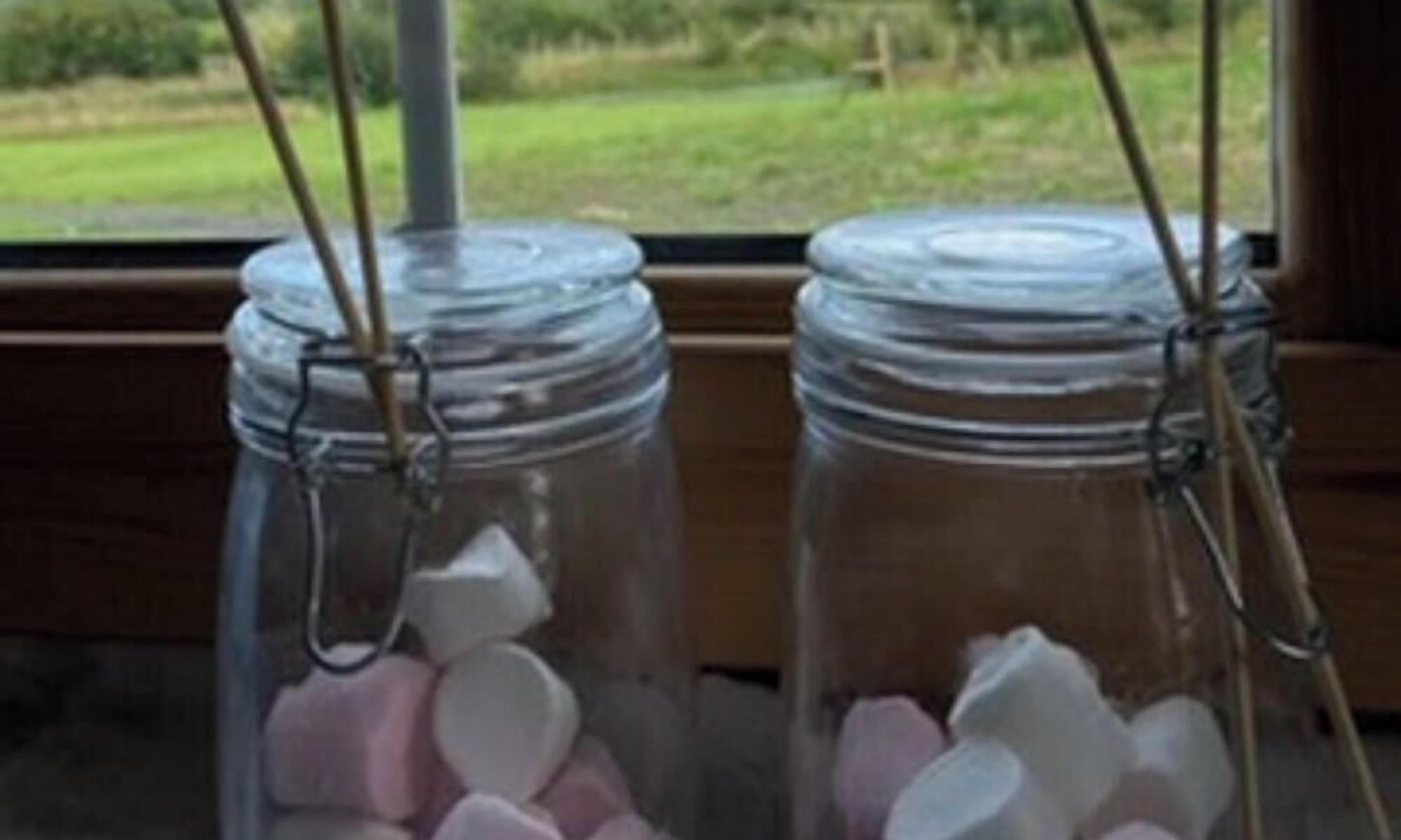 Two glass jars with metal clasps on a wooden surface, with a view of a green landscape through a window.