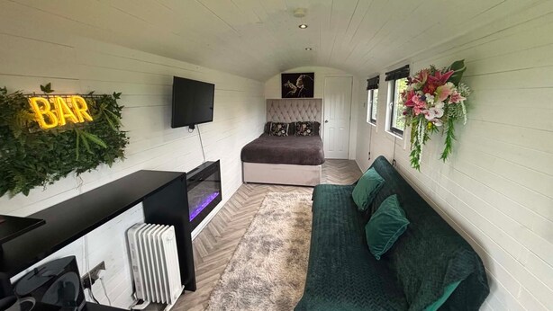 Ett litet rum med en säng, en soffa, en tv, ett element och en skylt med texten ”BAR”.