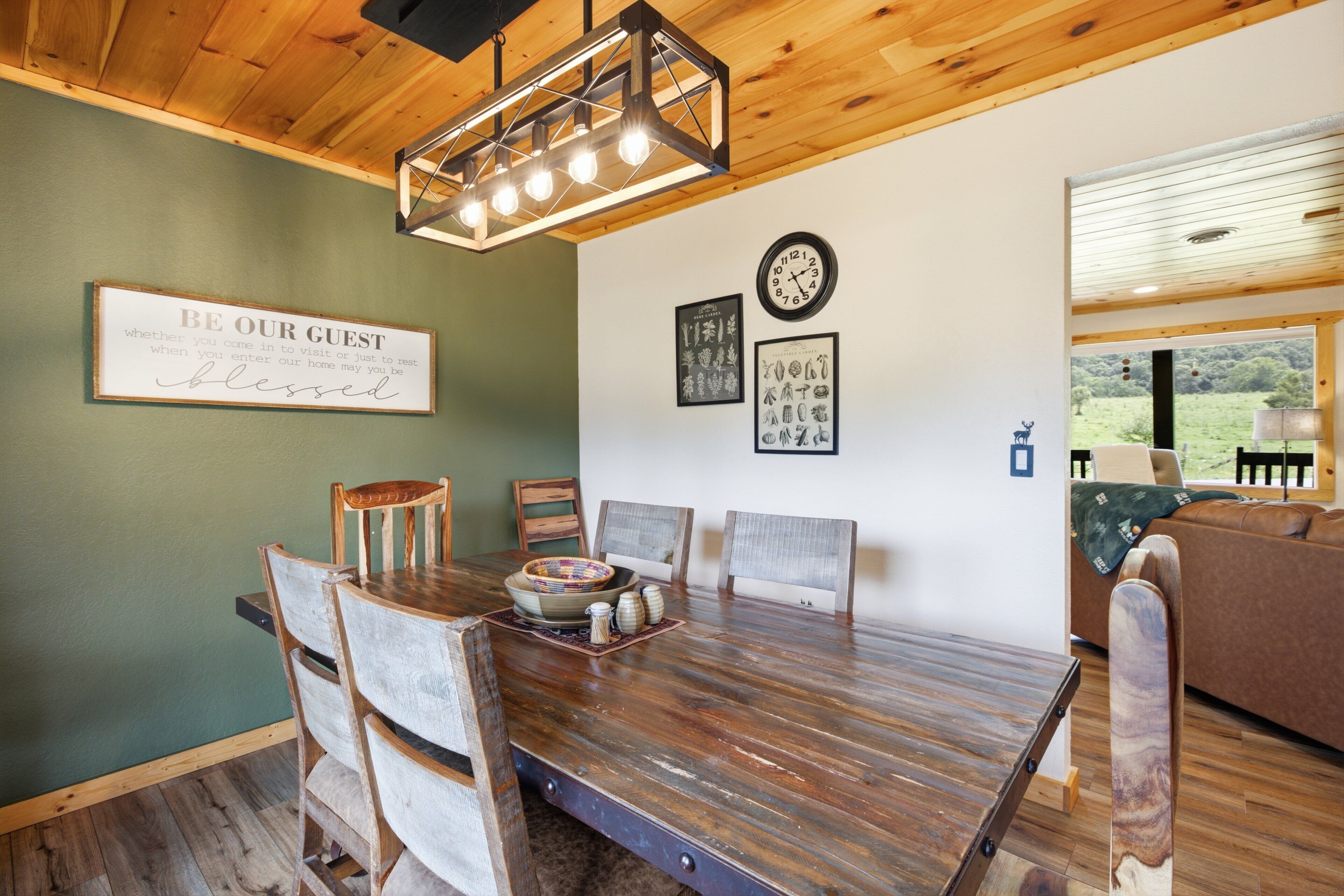 A dining area with a wooden table, chairs, a chandelier, framed pictures, and a clock on the wall.