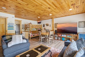 Una sala acogedora con techo de madera, un televisor, una cama litera y un comedor.