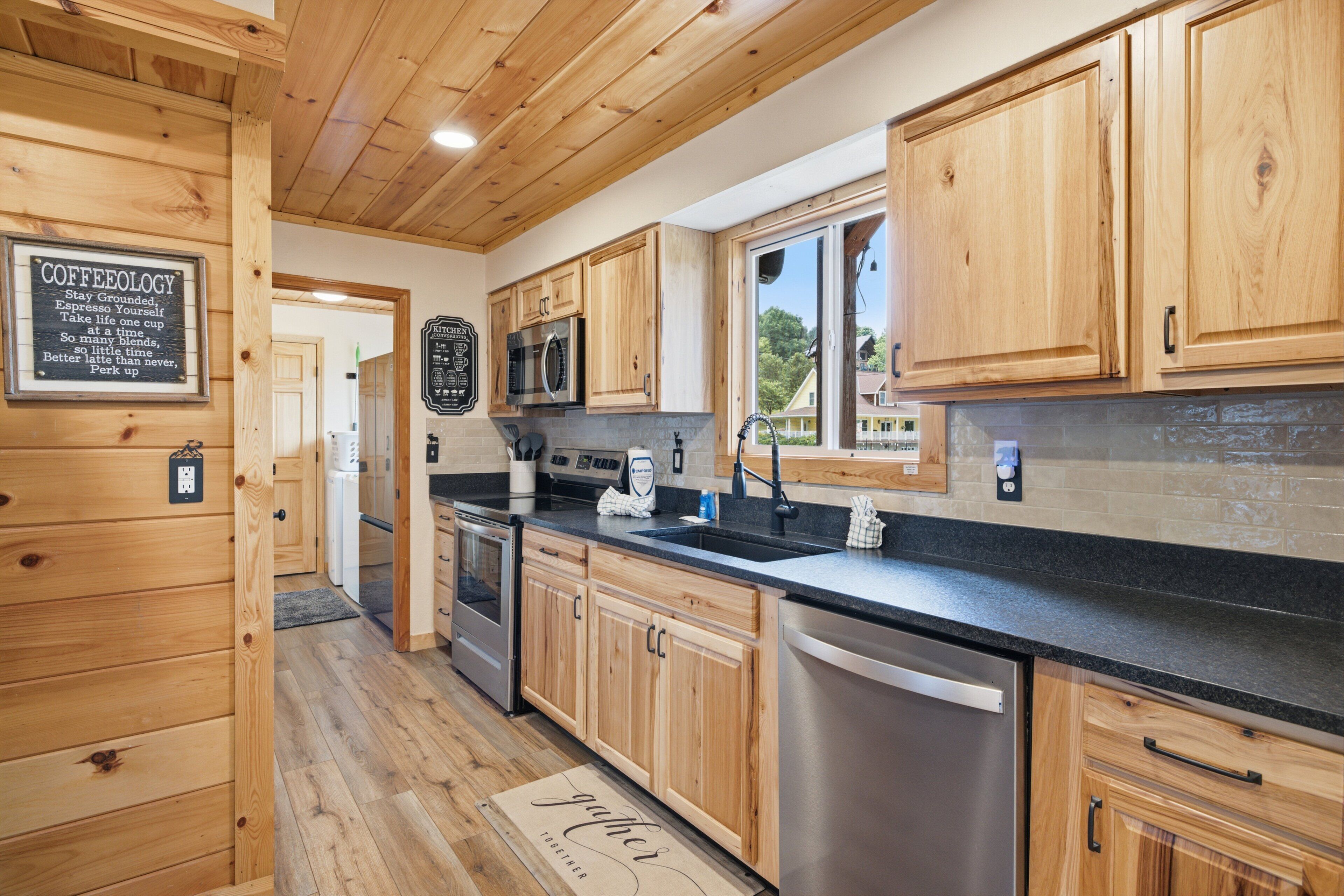 A kitchen with wooden cabinets, a stainless steel dishwasher, and a black countertop.