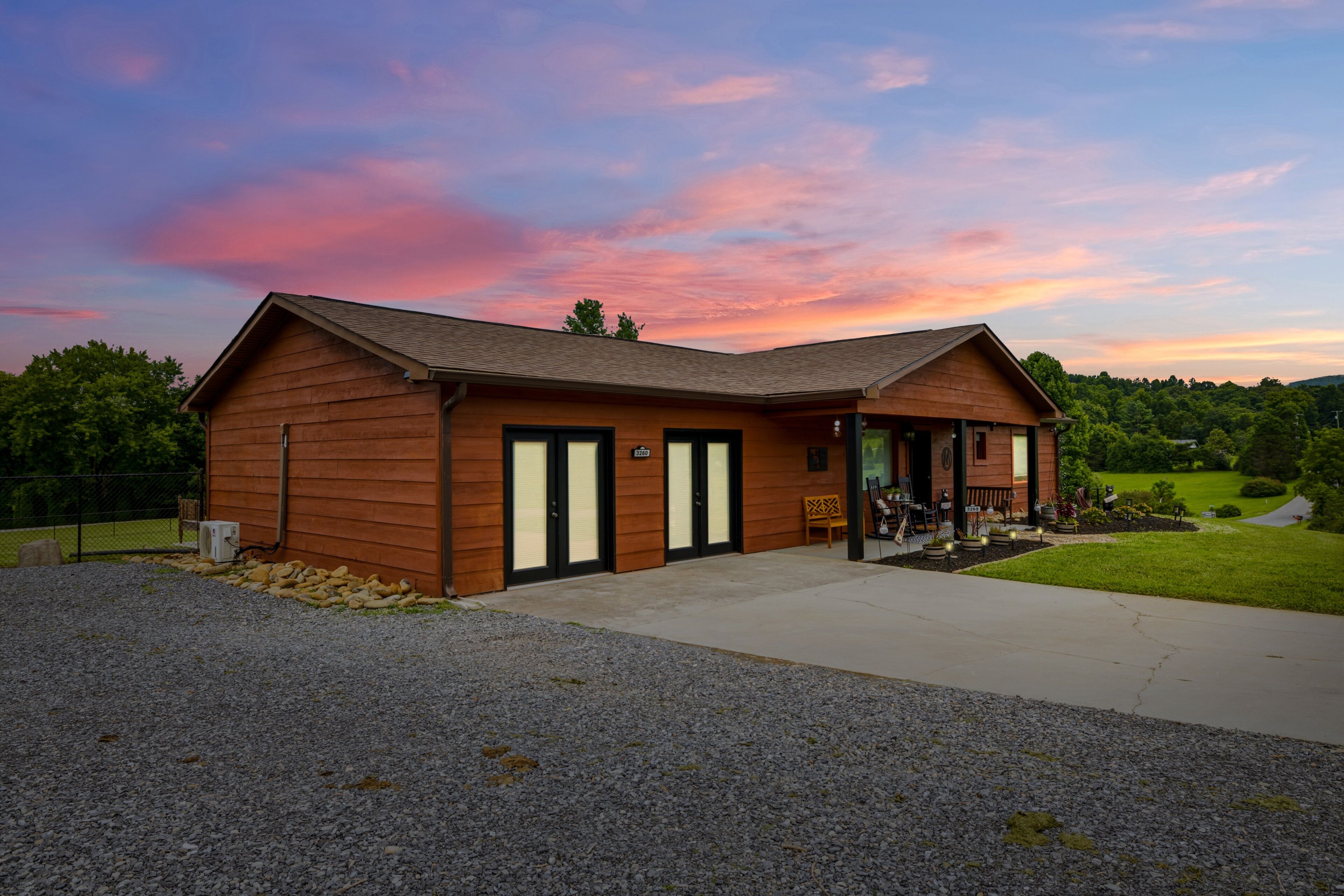 A wooden cabin with a covered porch, a gravel driveway, and a sign indicating the address.