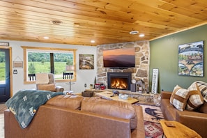 A cozy living room with a stone fireplace, leather sofas, a television, and a view of the outdoors. - Webster Lodge At Covemont 3 Bedroom Cabin (Sevierville)