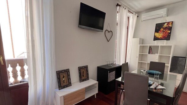 A modern living room with a flat-screen TV, a glass dining table, and a white console table with decorative items. - Apartment in downtown Valencia, close to everything (València)