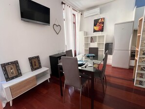 Un espacio habitable compacto con comedor, televisor montado en la pared, estantería y refrigerador.