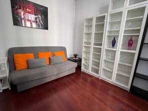 Ein Wohnzimmer mit grauem Sofa, orange-grauen Kissen, einer weißen Kommode mit Glastüren und einem gerahmten Bild an der Wand.