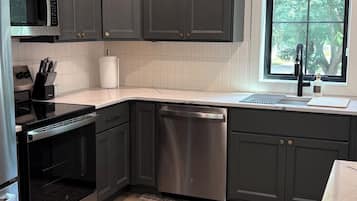 A modern kitchen with dark cabinets, a stainless steel dishwasher, and a window providing natural light.