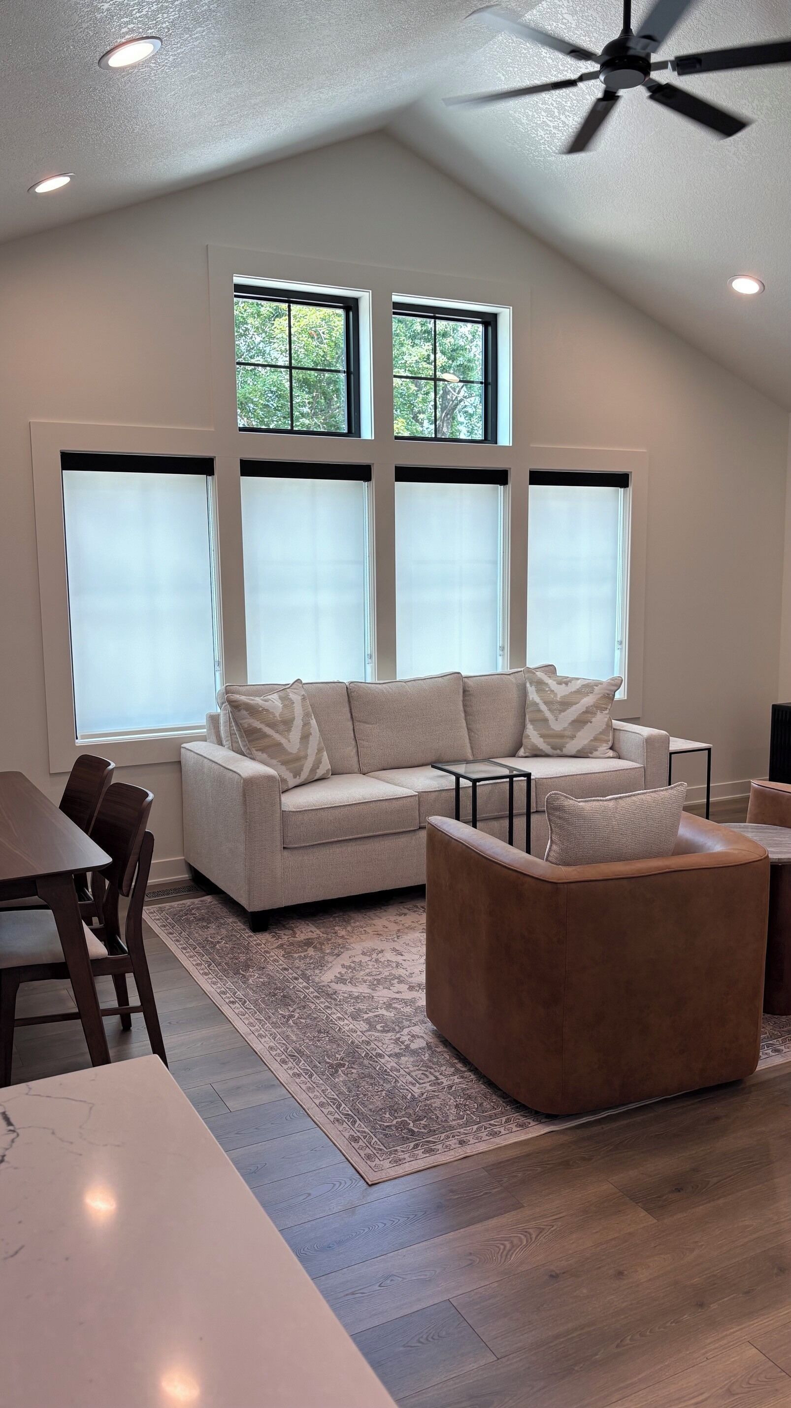 A modern living room with a sectional sofa, a brown ottoman, a glass coffee table, and a dining area with a table and chairs.