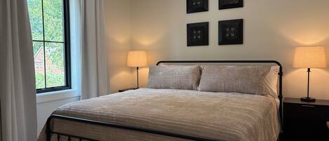 Quarto com uma cama, duas luminárias de cabeceira, uma janela com cortinas e quatro quadros pendurados na parede.