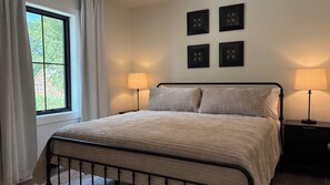 A bedroom with a bed, two bedside lamps, a window with curtains, and four wall-mounted picture frames. - Gezellig Carriage House - The Zuid Holland Suite - Pella's Premier Retreat (PELLA)