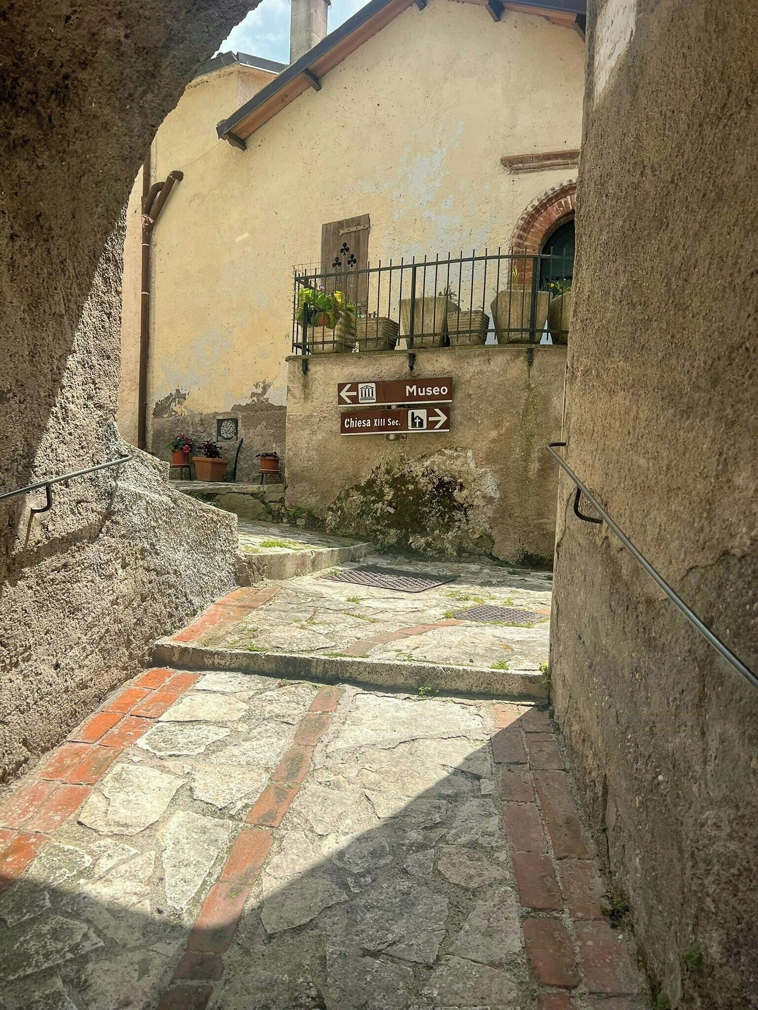 A narrow stone pathway leading to a building with a sign indicating directions to a museum and a church.