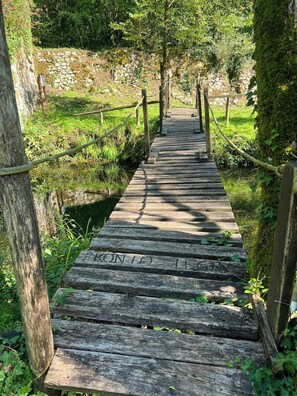 Un pont en bois, doté de garde-corps, entouré de verdure et bordé d’un mur de pierres.
