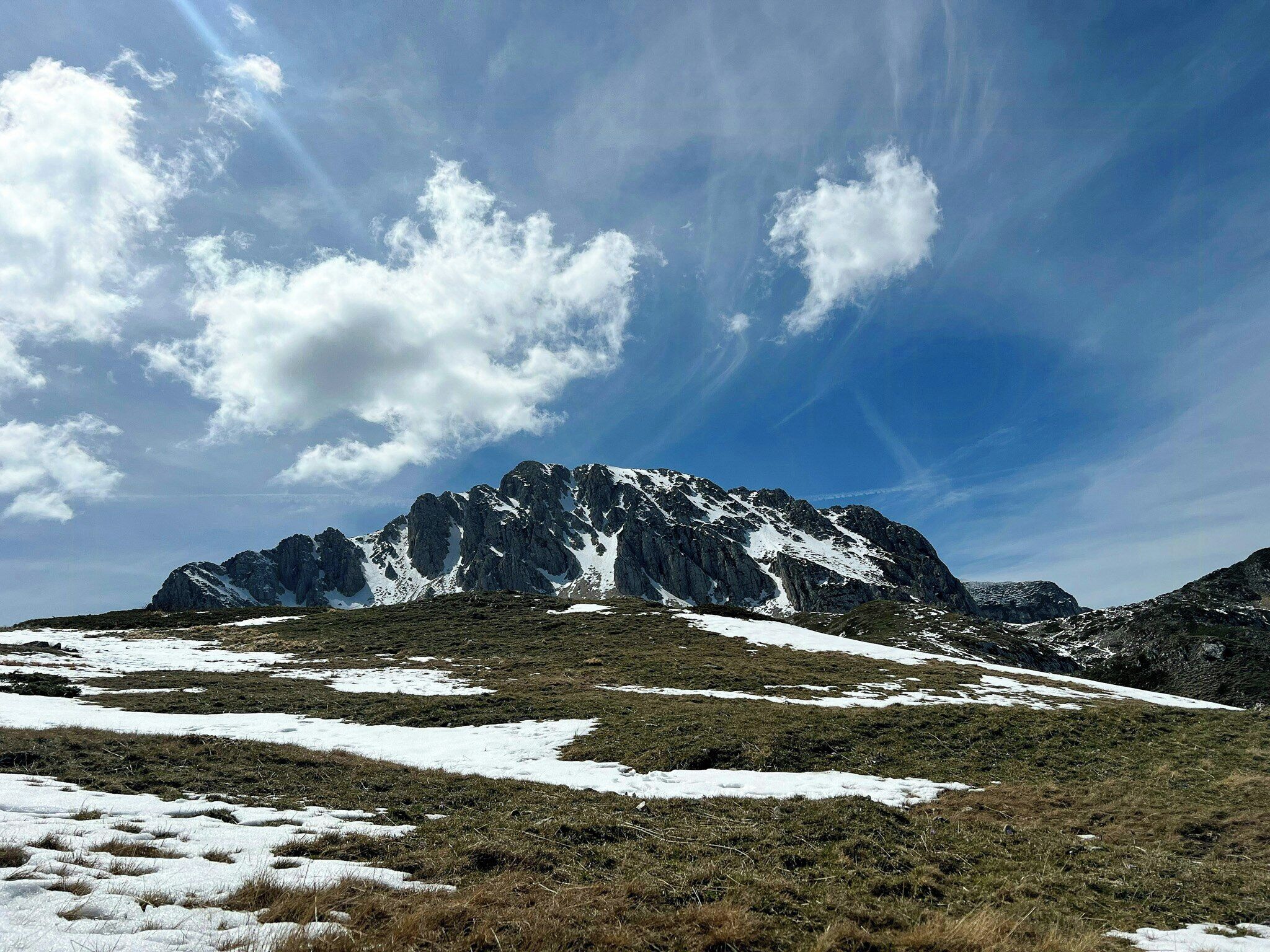 Un paysage montagneux parsemé de plaques de neige, sous un ciel dégagé.