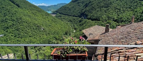 A terrace with terracotta roof tiles, a potted plant, and a view of a valley with lush greenery and a distant mountain.