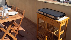 Eine Terrasse mit Tisch für zwei Personen, einem tragbaren Grill und Blick auf das Meer und die Hügel.