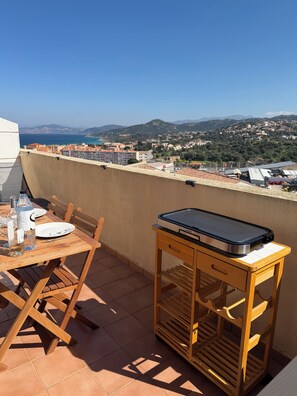 A terrace with a table set for two, a portable grill, and a view of the sea and hills. - L'Île Rousse - Two-bedroom apartment with a terrace offering views of the sea and mountains - 8-minute walk to the beach (L'Île-Rousse)