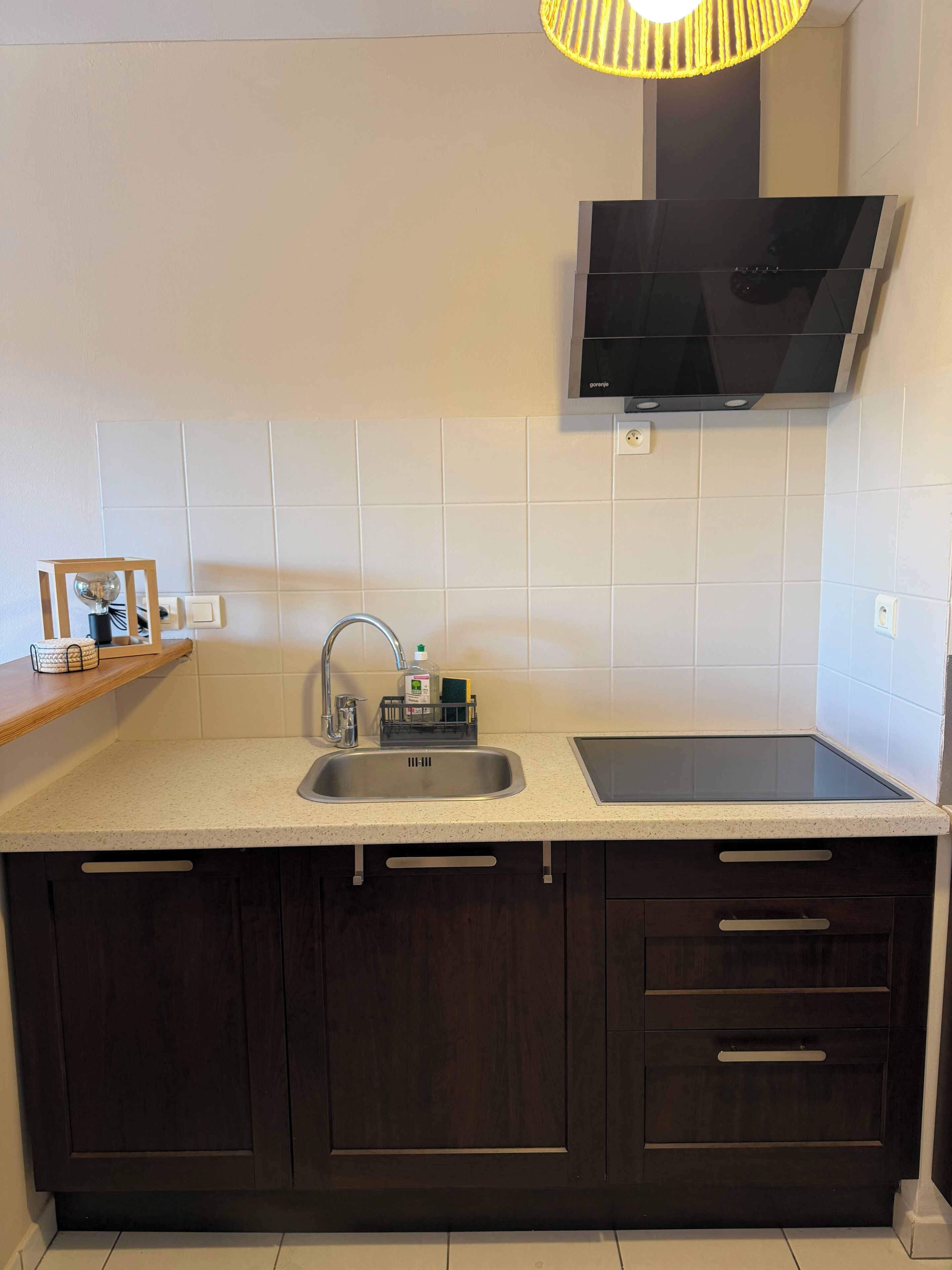 Eine moderne Küche mit Spüle aus Edelstahl, integriertem Herd, dunklen Holzschränken und einem an der Wand montierten Fernseher.