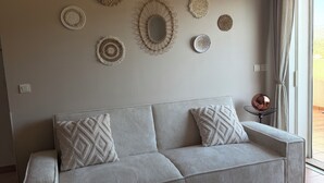 Ein modernes Wohnzimmer mit einer Couch, Wanddekoration, einer Deckenleuchte und Blick durch ein Fenster.