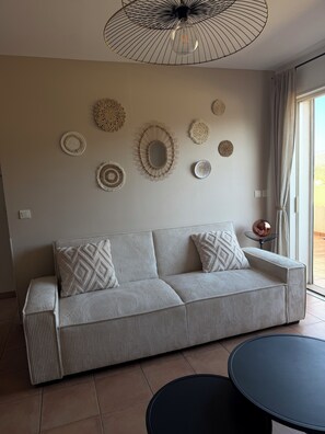 A modern living room with a sofa, decorative wall art, a ceiling light fixture, and a view through a window. - L'Île Rousse - Two-bedroom apartment with a terrace offering views of the sea and mountains - 8-minute walk to the beach (L'Île-Rousse)