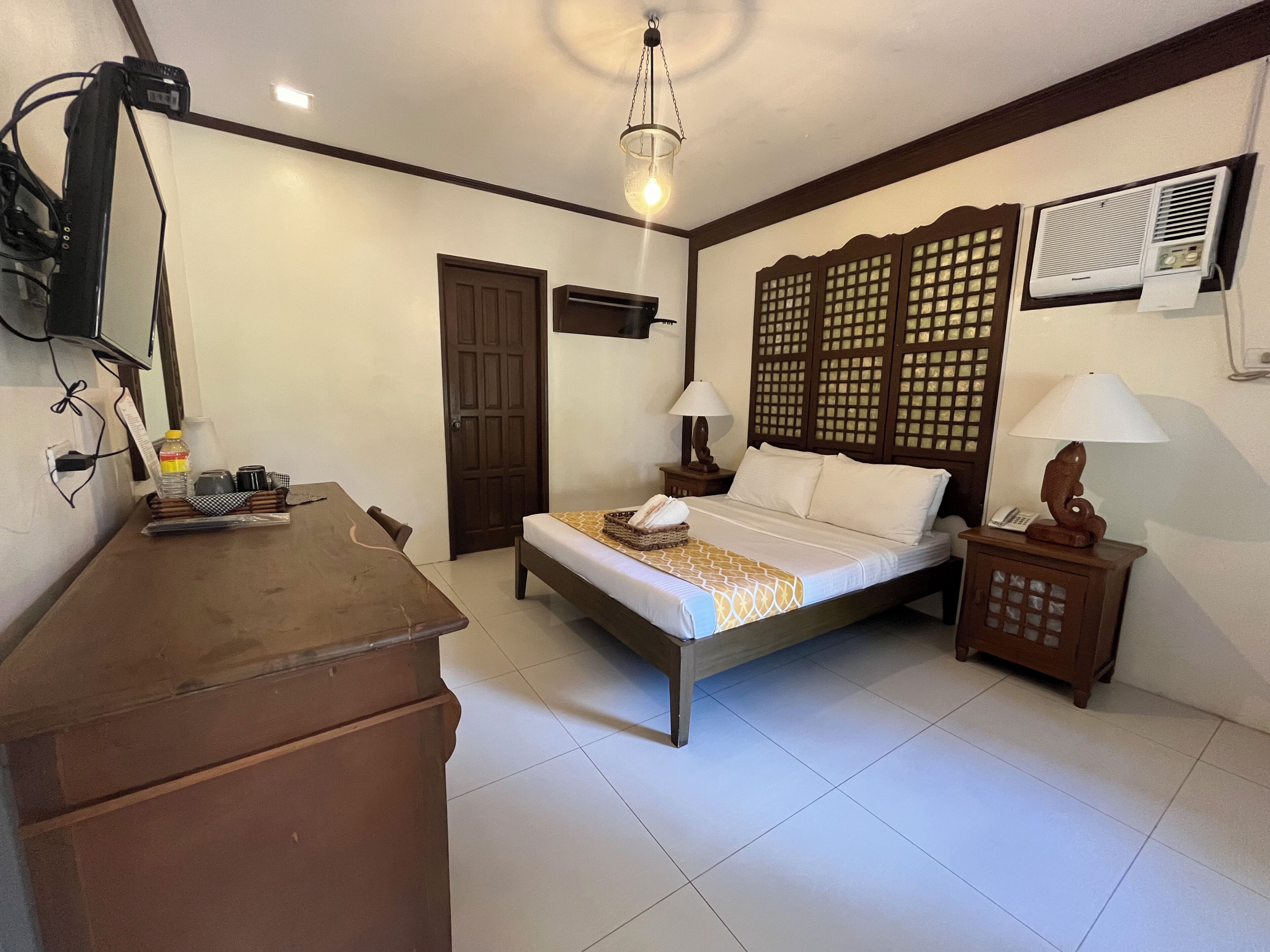 A bedroom with a bed, bedside table, lamp, and a TV mounted on the wall.