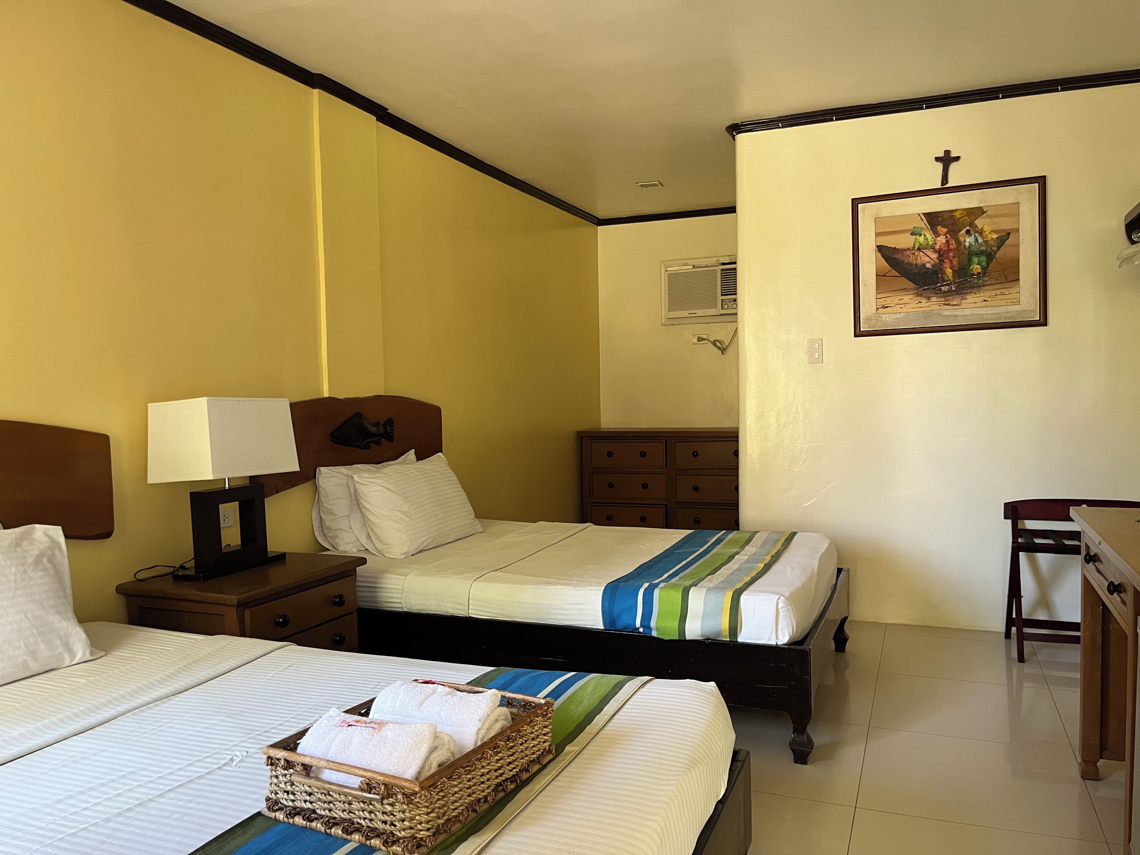 A hotel room with two beds, a nightstand with a lamp, a dresser, a framed picture on the wall, and a small table.