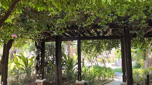 A covered walkway with brick pillars and a tiled floor, surrounded by lush greenery and potted plants. - Puerto Del Sol Beach Resort and Hotel Club Bolinao (Bolinao)
