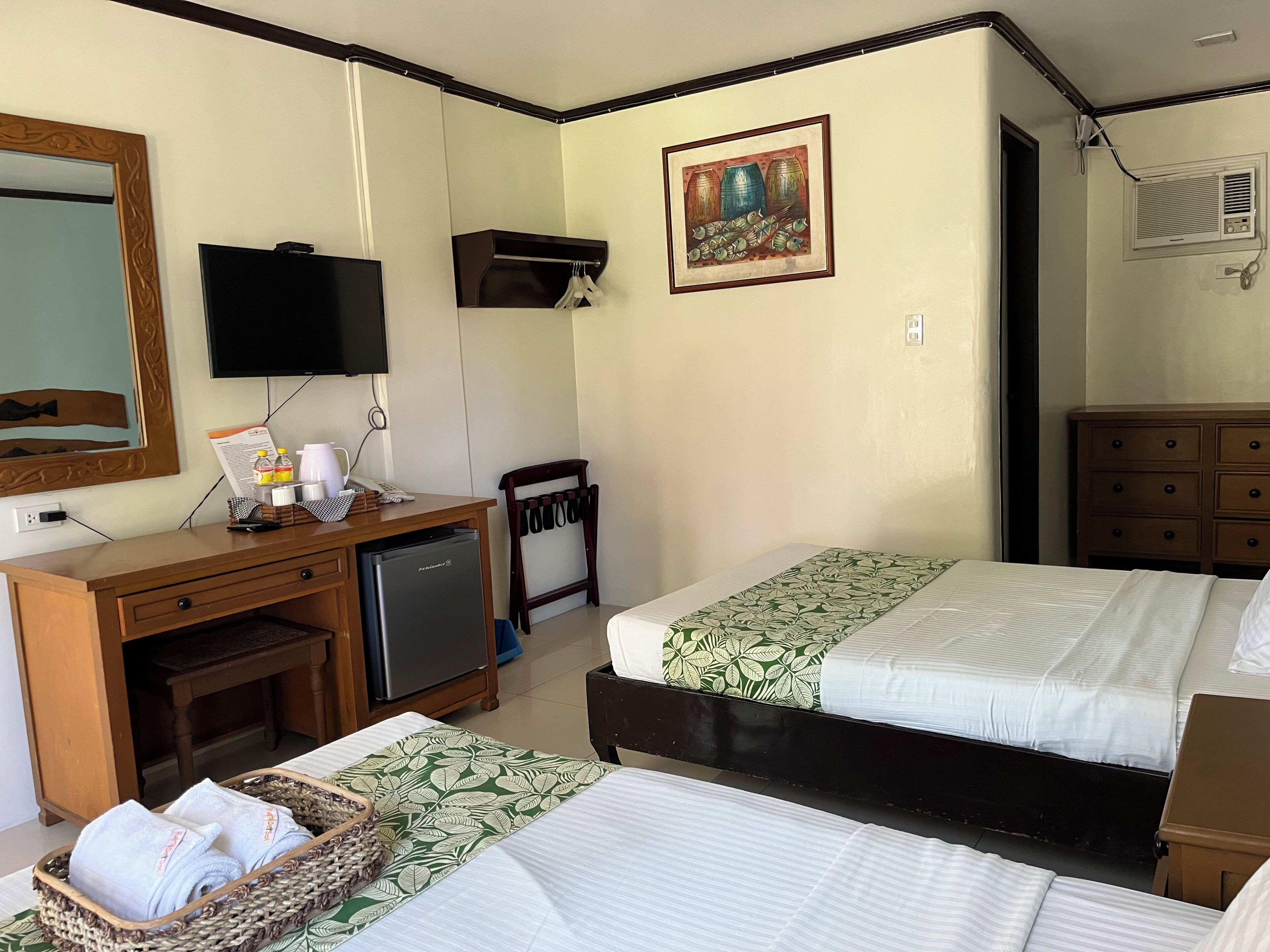 A hotel room with two beds, a desk with a refrigerator, a television, and a painting on the wall.