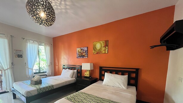 A hotel room with two beds, a window with curtains, a wall-mounted artwork, and a hanging light fixture. - Puerto Del Sol Beach Resort and Hotel Club Bolinao (Bolinao)