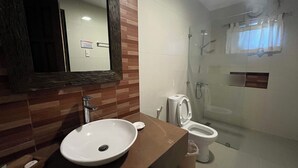 A bathroom with a wooden vanity, a white sink, a toilet, and a glass-enclosed shower area. - Puerto Del Sol Beach Resort and Hotel Club Bolinao (Bolinao)