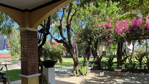 An outdoor patio area with a brick column, a potted plant, and a view of a well-maintained lawn and trees. - Puerto Del Sol Beach Resort and Hotel Club Bolinao (Bolinao)