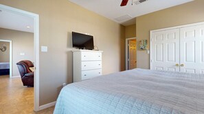 Un dormitorio con cama, cómoda, televisor y puerta que da a otra habitación.