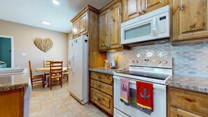 A kitchen with wooden cabinets, a microwave, an oven, and a dining area with a table and chairs. - Turtlely Relaxed: 3  BR, 2  BA House in Crystal Beach, Sleeps 10 (Crystal Beach)