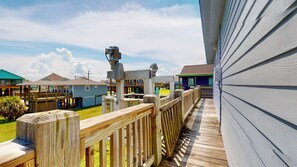 A wooden deck with a view of a residential area, including houses and a grassy field. - Turtlely Relaxed: 3  BR, 2  BA House in Crystal Beach, Sleeps 10 (Crystal Beach)